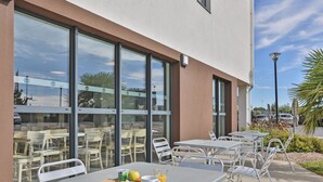 An outdoor seating area with tables and chairs, a glass door entrance, and a clear sky.