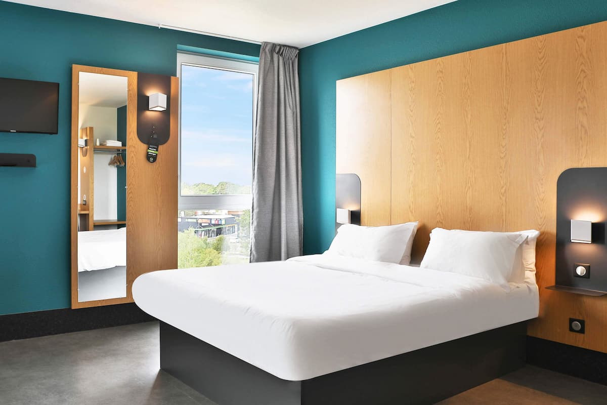 Ein modernes Hotelzimmer mit einem großen Bett, einem Holzkopfteil, einem großen Fenster mit Blick und einem beleuchteten Spiegel.