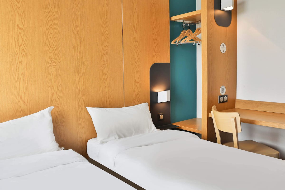 Ein Hotelzimmer mit zwei Betten, einem Schreibtisch, einem Stuhl und einem Kleiderschrank mit Kleidung.