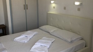 Un lit bien fait, avec du linge de lit et des serviettes blanches, une tête de lit rembourrée et deux appliques murales.