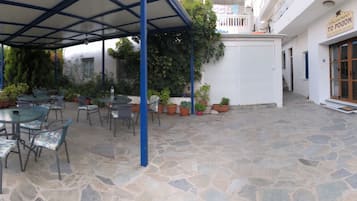 Un patio al aire libre con piso de piedra, mesas y sillas de metal, y plantas en macetas.