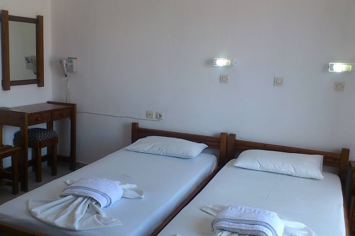 Una habitación sencilla con dos camas individuales, un escritorio de madera, una silla, un teléfono e iluminación empotrada.