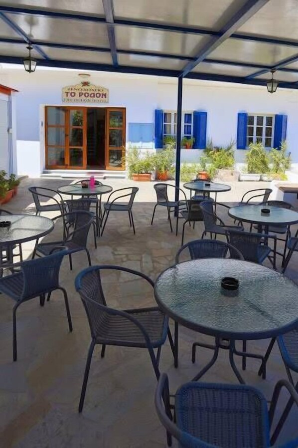 An outdoor patio area with round tables and chairs, a covered seating area, and a building entrance with a sign.