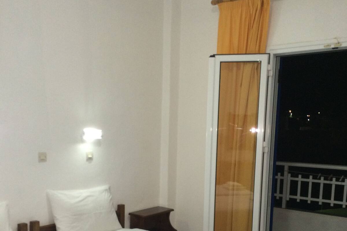 Habitación de hotel con dos camas, una mesita de noche, una puerta corrediza de vidrio a un balcón y una lámpara fijada a la pared.