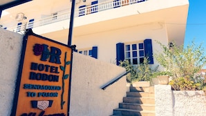 L’entrée d’un hôtel, avec une enseigne, un escalier et un ciel bleu dégagé.