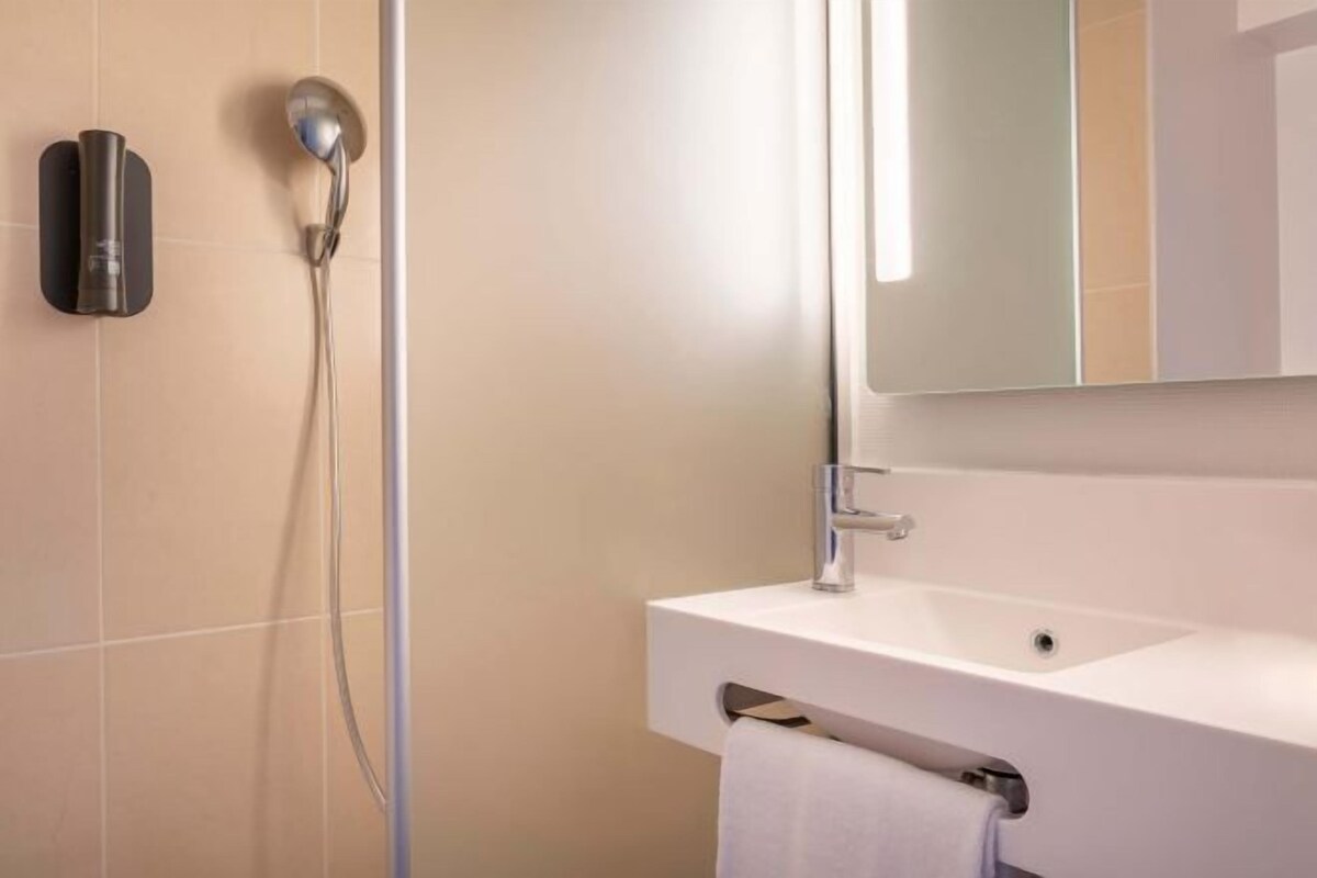 Un baño moderno con un lavamanos blanco, un espejo y un cabezal de ducha.