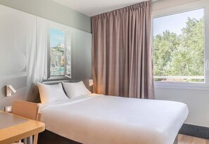 Una camera d'albergo con un letto, una scrivania e una finestra con tende.