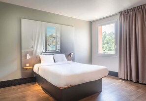 Une chambre d’hôtel moderne avec un grand lit, une table de chevet, une lampe fixée au mur et une fenêtre avec des rideaux.