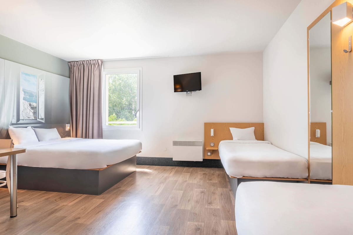 A hotel room with two beds, a TV, a window with curtains, and a wooden floor.