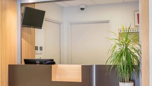 A reception desk with a flat-screen TV, a Dell computer, and a potted plant. - B&B HOTEL Marseille Aéroport Saint-Victoret (Saint-Victoret)