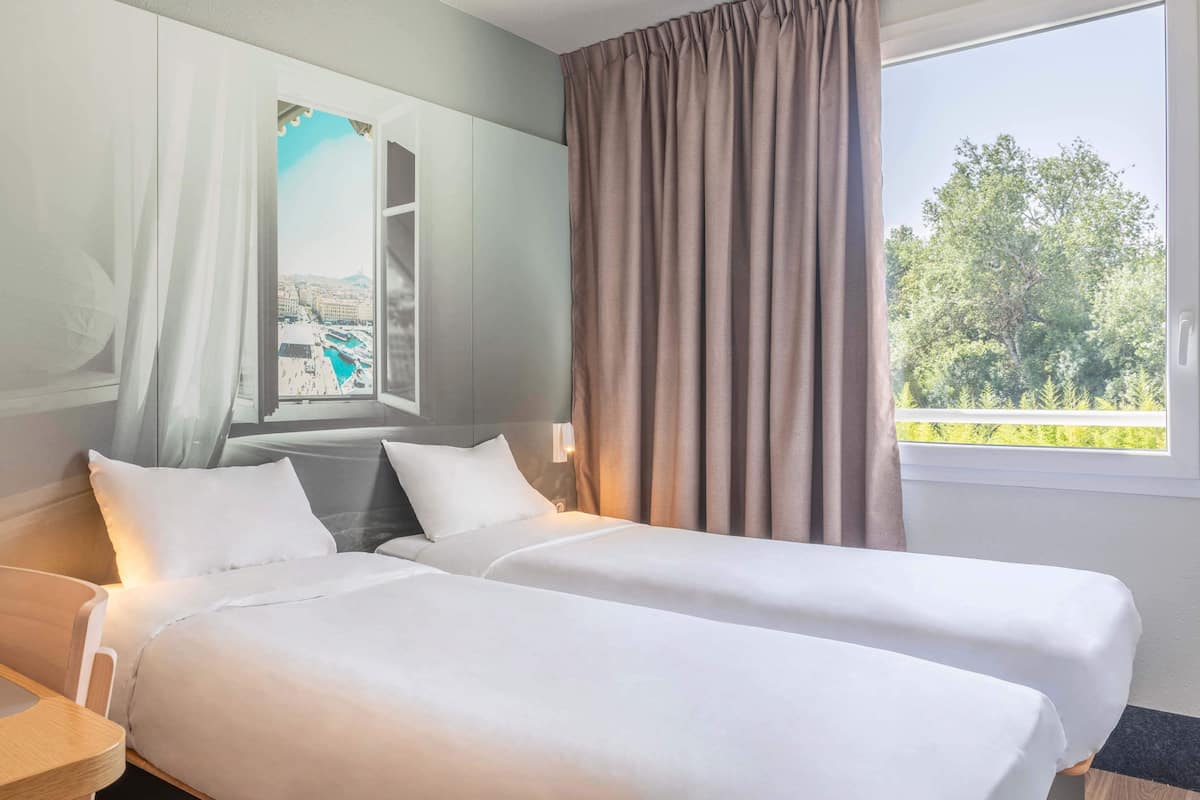 A hotel room with two beds, a large window with curtains, and a view of a cityscape.
