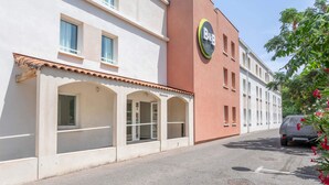 A hotel with a B&B sign, a covered outdoor seating area, and a parked car. - B&B HOTEL Marseille Aéroport Saint-Victoret (Saint-Victoret)