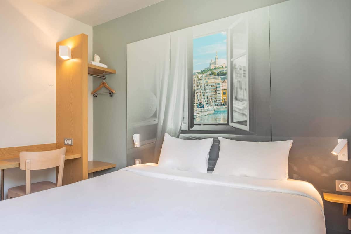 A hotel room with a bed, a desk, and a chair. There is a window with a view of a cityscape.