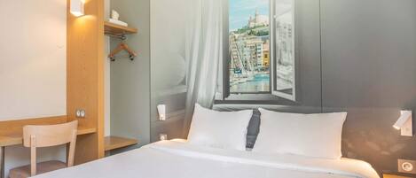 Habitación de hotel con cama, escritorio y silla. Ventana con vista a paisaje urbano.