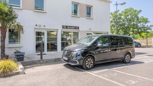 A black Mercedes-Benz van parked in front of a building with a sign reading "Accueil" and a palm tree nearby. - B&B HOTEL Marseille Aéroport Saint-Victoret (Saint-Victoret)