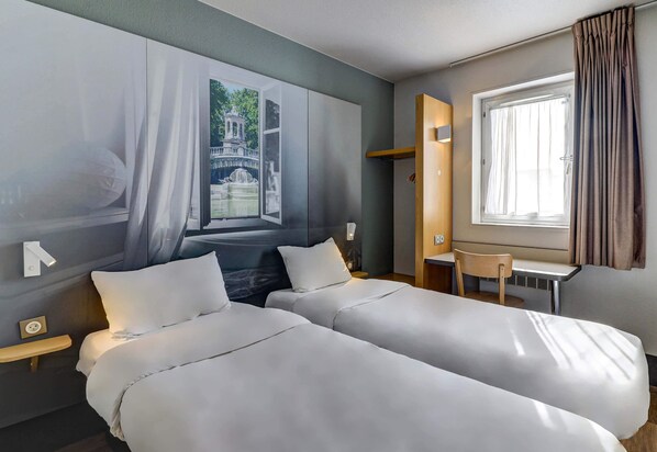 A hotel room with two beds, a small desk, a window with curtains, and a wall-mounted light. - B&B HOTEL DIJON Nord (Dijon)
