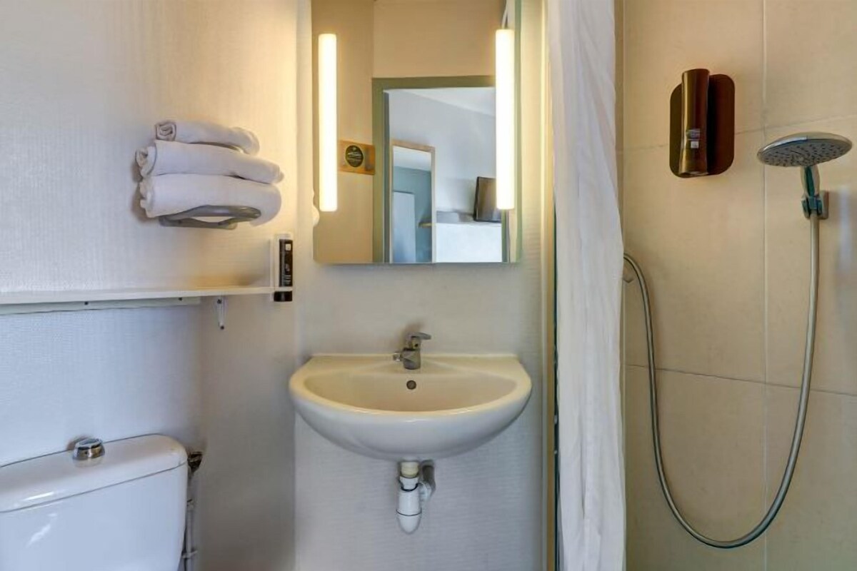 Une salle de bain avec un lavabo blanc, un miroir, des toilettes et une douche.