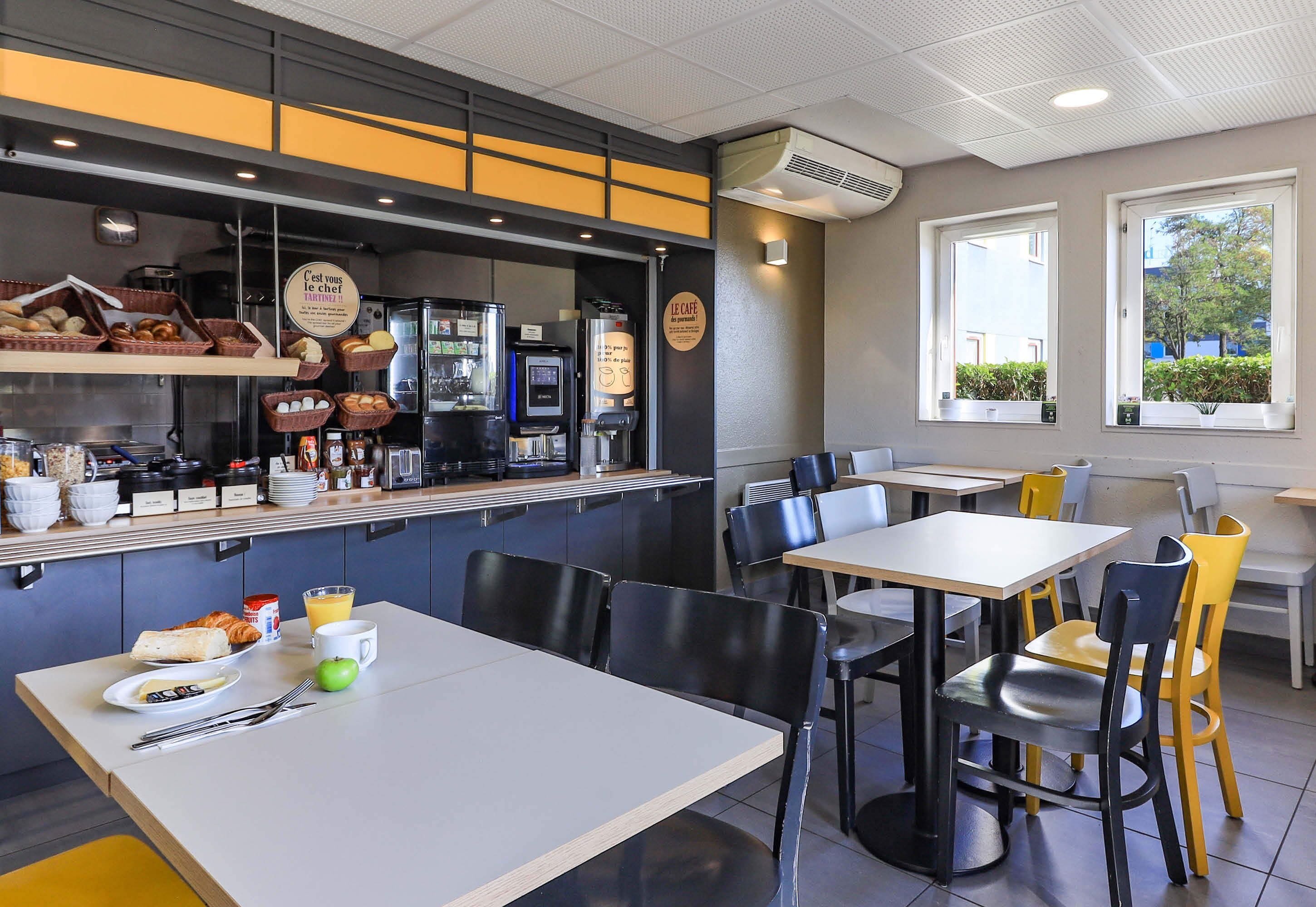 Un café con un mostrador que exhibe comida y bebidas, mesas y sillas, y vistas al exterior a través de ventanas.