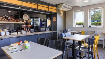 Un café con un mostrador que exhibe comida y bebidas, mesas y sillas, y vistas al exterior a través de ventanas.