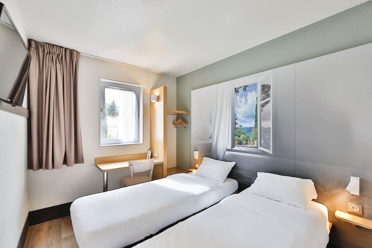 Una habitación de hotel con dos camas, un escritorio y una ventana con cortinas.