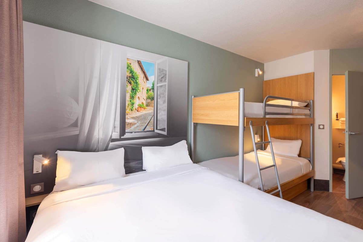 Habitaci ón de hotel con una cama grande, una cama litera, una ventana con vista a la calle y una mesita de noche con lámpara.