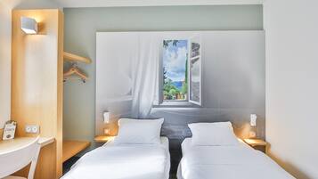Een hotelkamer met twee bedden, een bureau en een groot raam met uitzicht op groen.