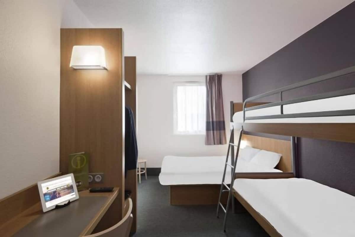 Een hotelkamer met een stapelbed, een bureau met een tablet, een lamp en een raam met gordijnen.