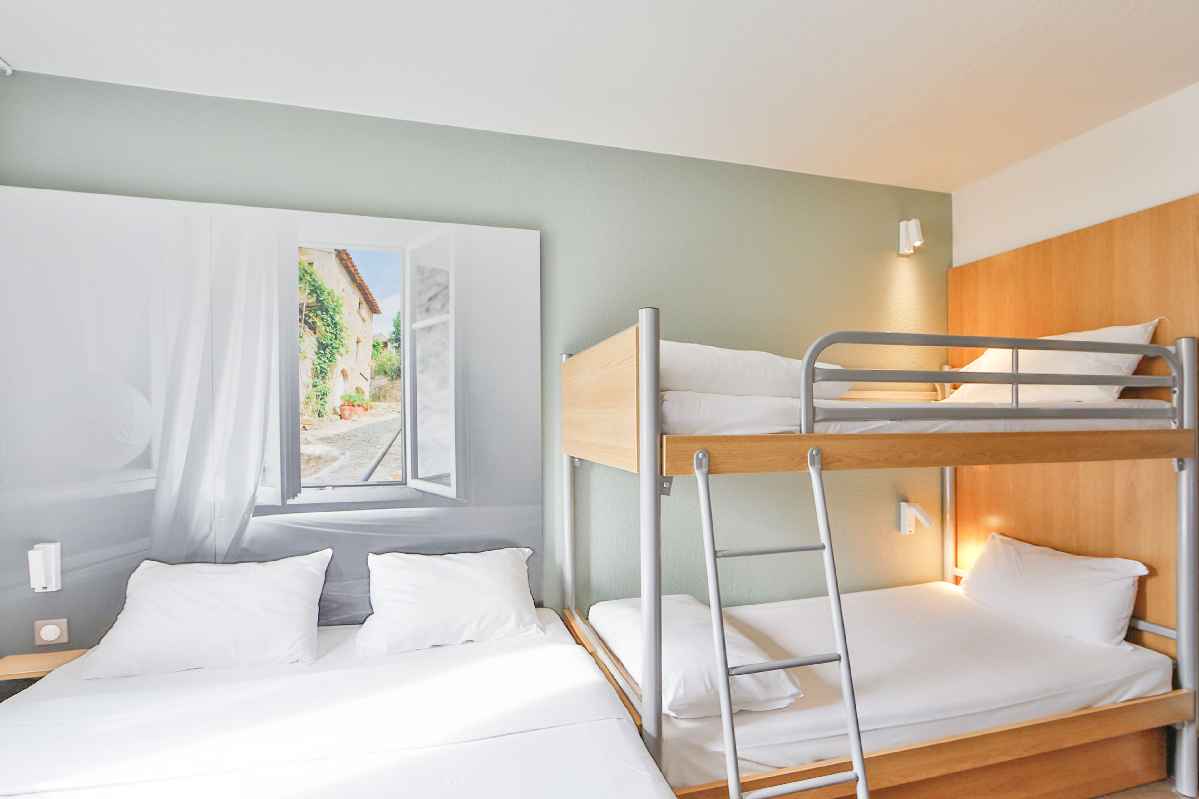 A bunk bed room with a painting on the wall, a bedside table, and a nightstand.