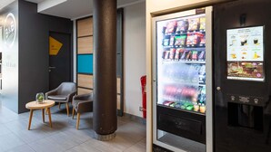 Un vestíbulo de hotel con una máquina expendedora, zona de estar y un pilar.