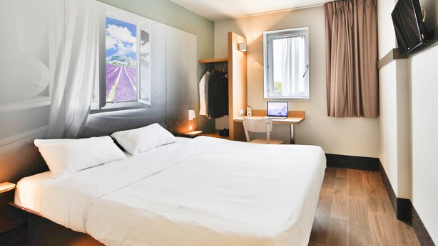 Una habitación de hotel con una cama grande, un escritorio con ordenador, un armario y una ventana con cortinas.