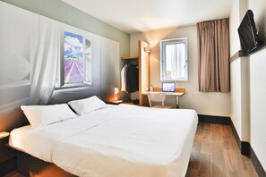 Una habitación de hotel con una cama grande, un escritorio con ordenador, un armario y una ventana con cortinas.