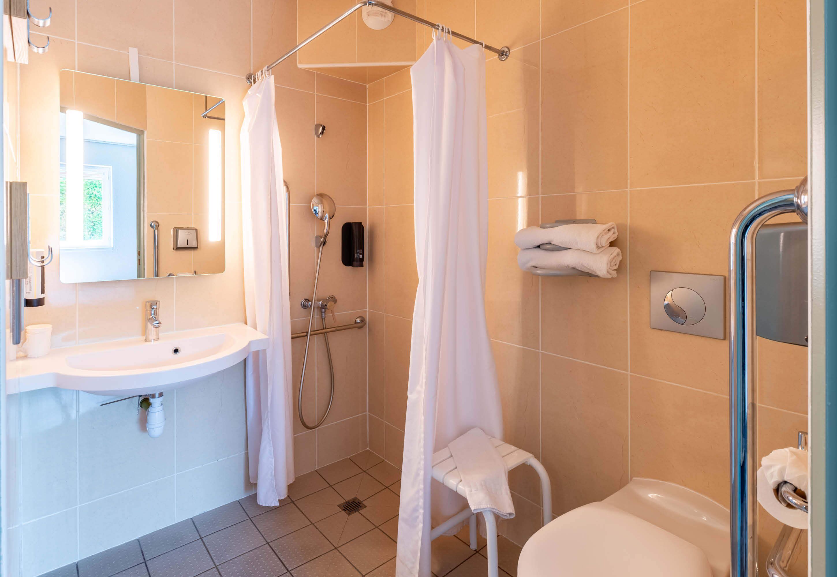 Un baño moderno con lavamanos, espejo, ducha e inodoro.