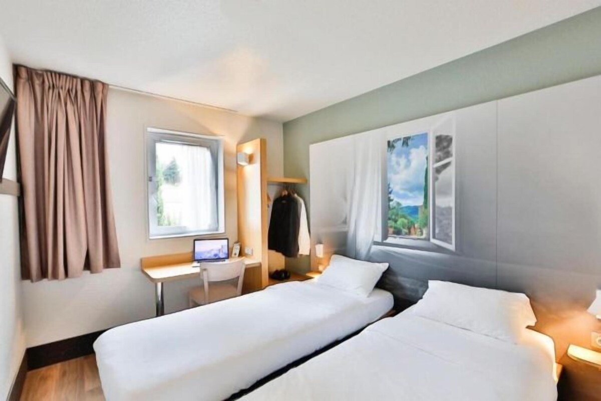 Een hotelkamer met twee bedden, een bureau, een computer en een raam met gordijnen.