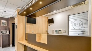 Un comptoir d’accueil avec une pancarte « Bienvenue », le logo de B&B Hotels, un téléviseur à écran plat et un écran numérique.