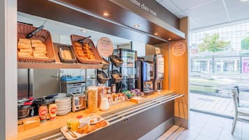 A breakfast buffet area with baskets of bread, a coffee machine, and various food items.