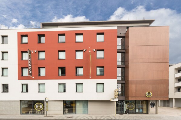 A modern hotel building with a red and white facade, multiple windows, and a B&B logo.