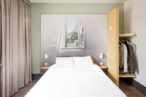 A bedroom with a bed, a nightstand, a wooden wardrobe, and a view of a building through an open window. - B&B HOTEL Mulhouse Centre (Mulhouse)