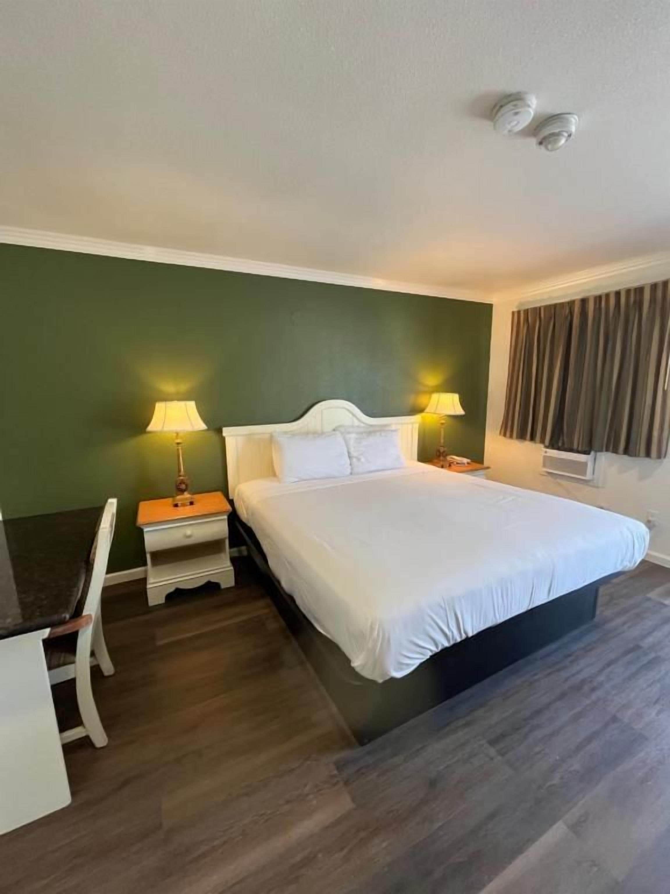 Una habitación de hotel con cama, lámparas de noche, escritorio y ventana con cortinas.