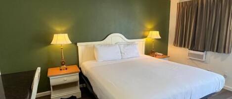Una habitación de hotel con cama, lámparas de noche, escritorio y ventana con cortinas.