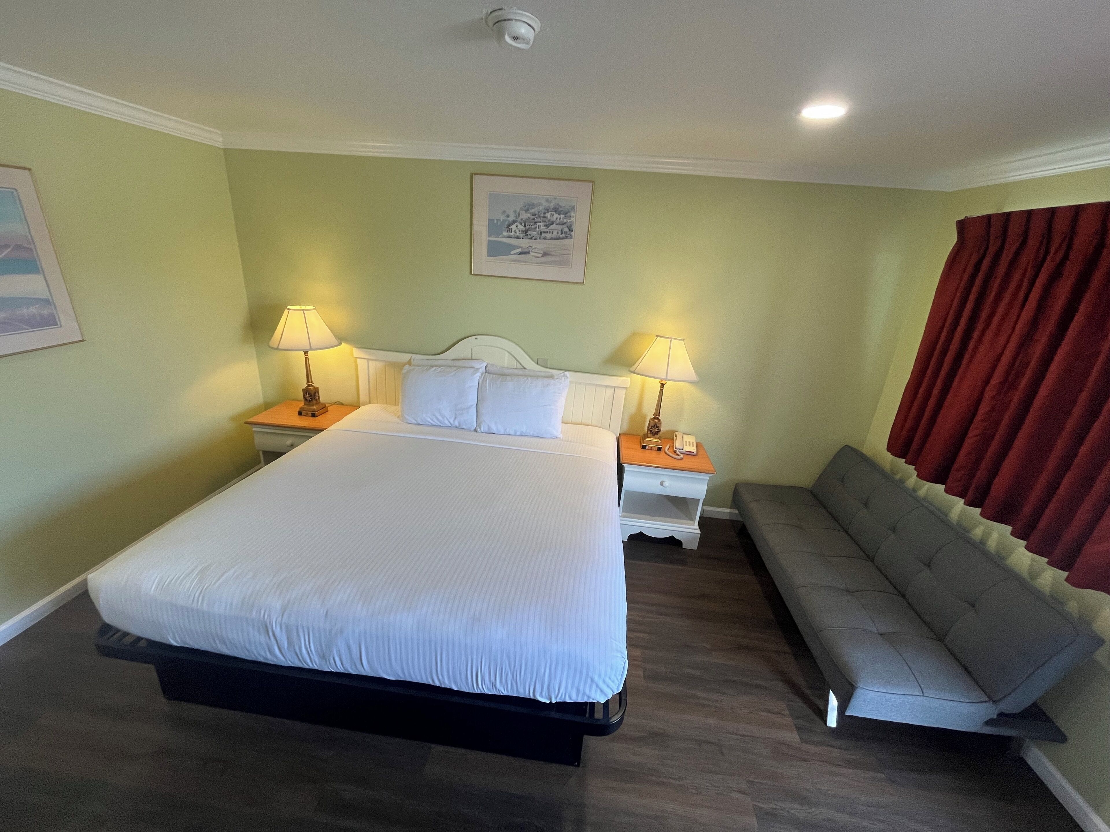 A hotel room with a large bed, two bedside tables with lamps, a grey sofa, and a painting on the wall.