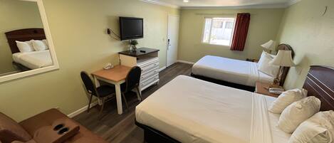 A hotel room with a bed, a desk with a chair, a television, and a window with curtains.