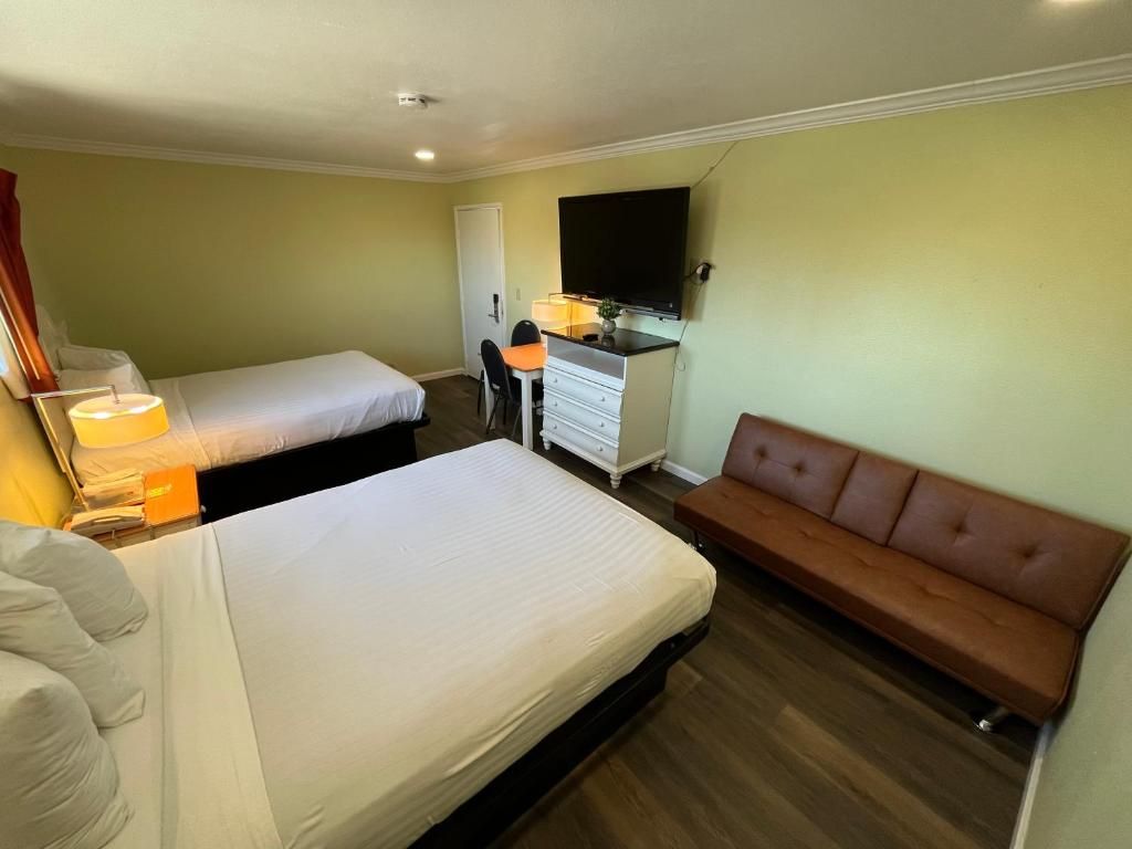 Una habitación de hotel con dos camas, un escritorio, una silla, un televisor y un sofá.