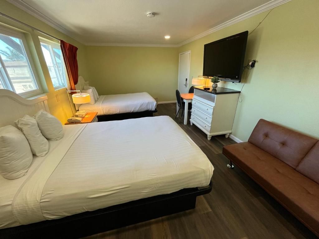 A hotel room with two beds, a desk, a television, and a sofa.