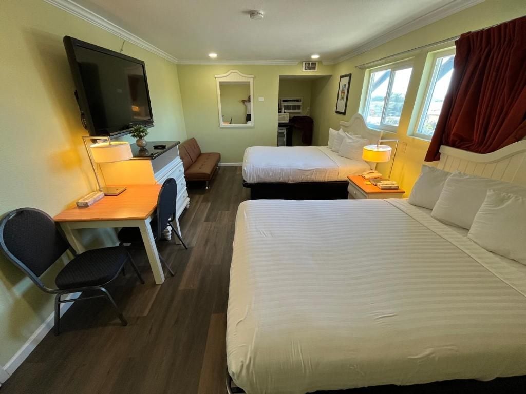 Une chambre d’hôtel avec deux lits, un bureau avec une chaise, une télévision et une fenêtre avec des rideaux.