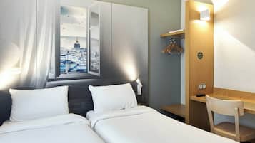 Une chambre d’hôtel comprenant un lit, un bureau avec une chaise, un porte-manteau et un luminaire fixé au mur.