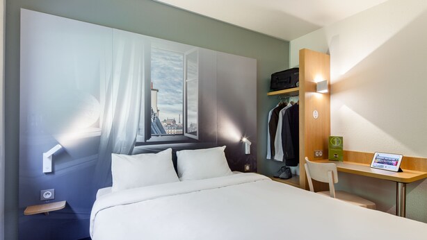 Habitación de hotel con cama, escritorio, silla, armario y televisor instalado en la pared.