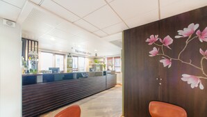 Un área de recepción con un mostrador de madera, dos sillas marrones y una pared con un diseño floral.