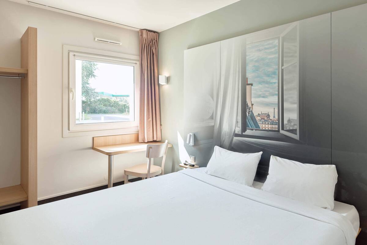 Une chambre d’hôtel avec un grand lit, un bureau, une chaise et une fenêtre avec des rideaux.