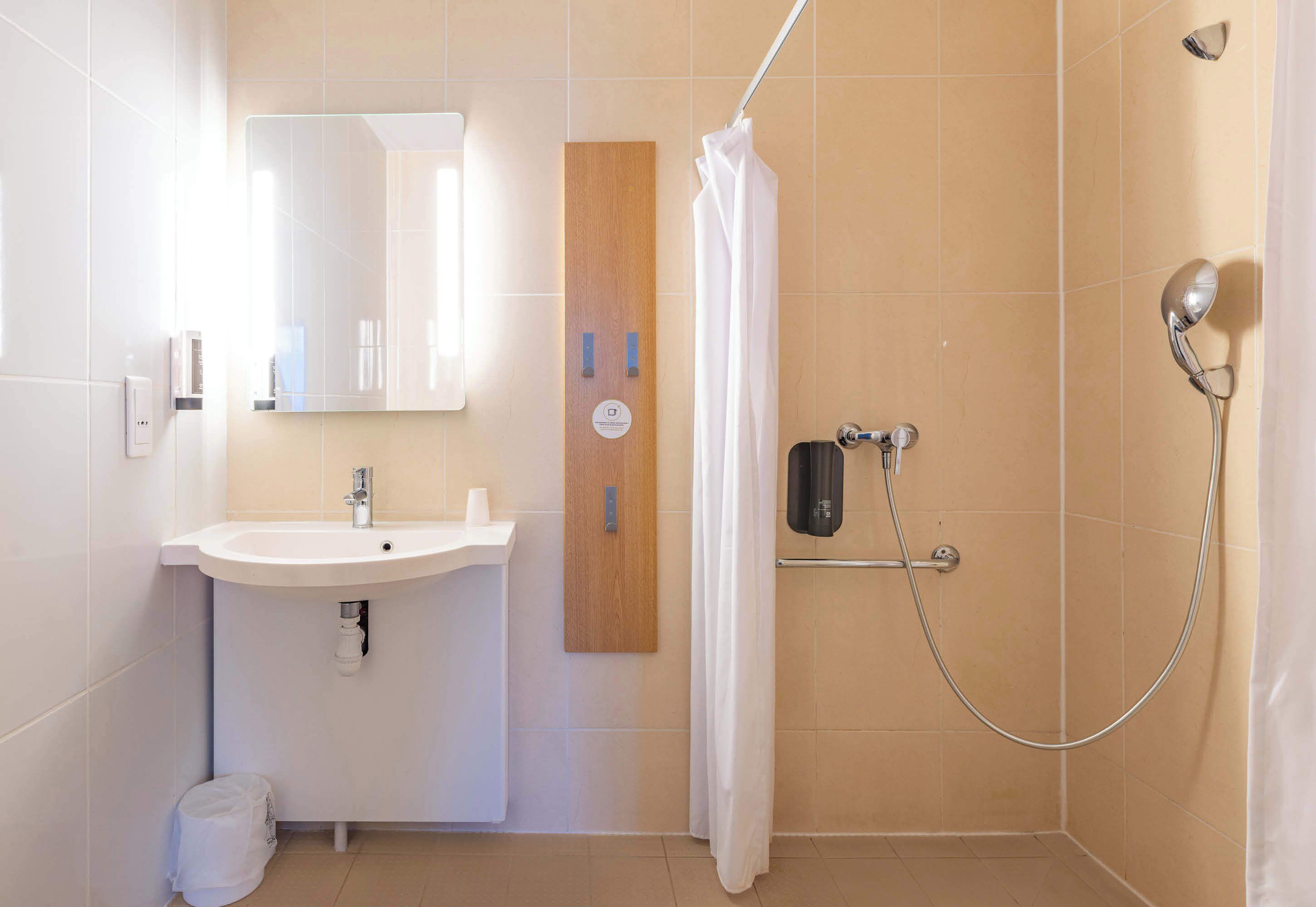 Ein Badezimmer mit Waschbecken, Spiegel, Dusche und Handtuchspender.