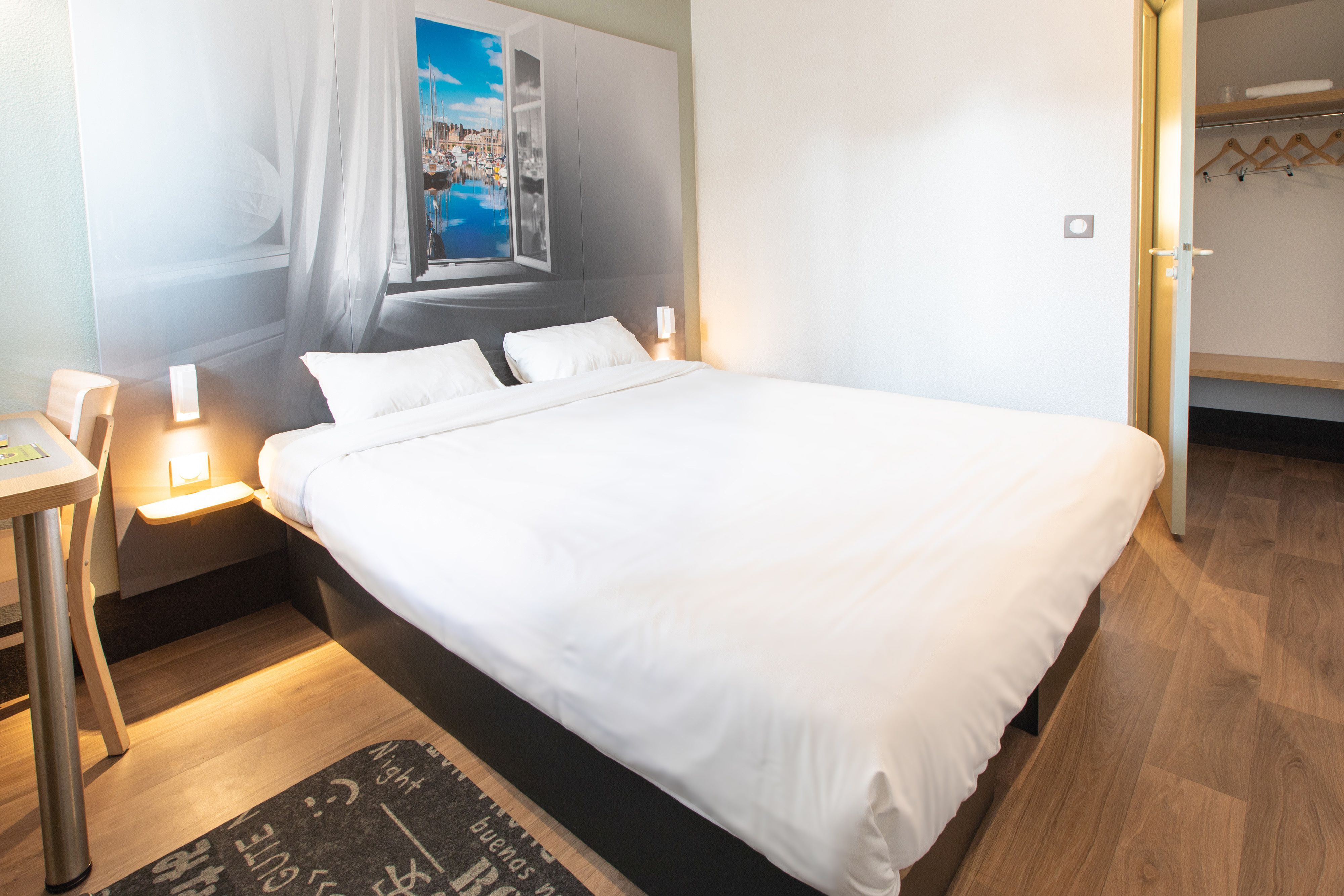 Ein Hotelzimmer mit einem großen Bett, Nachttischen mit Lampen, Blick auf eine Stadtansicht durch ein Fenster und einem Holzboden.